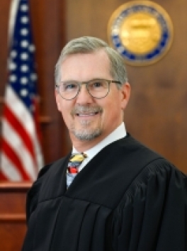 Photo of white male Judge standing in front of US Flag and Colorado State Seal